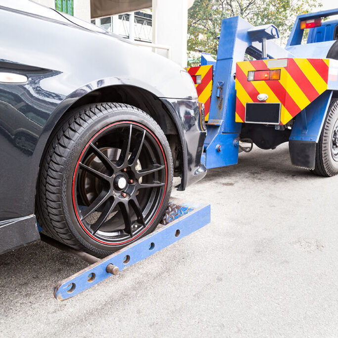 Tow truck towing a broken down car on the street.